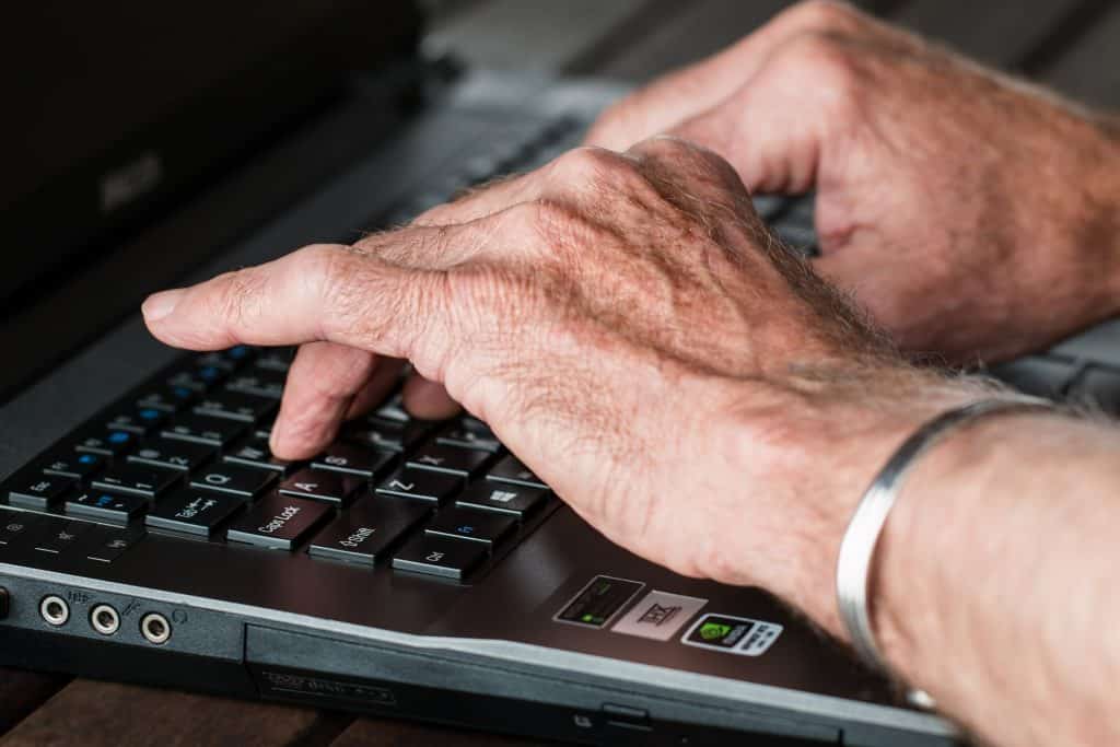 Imagem das mãos de uma pessoa idosa digitando em um notebook.