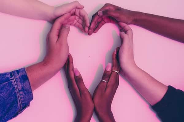 Mãos unidas formando um coração com fundo rosa