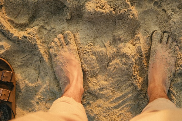 Pés descalços na areia vistos de cima