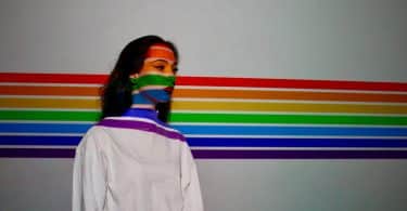 Mulher ao lado de uma parede que está refletindo as cores do arco íris