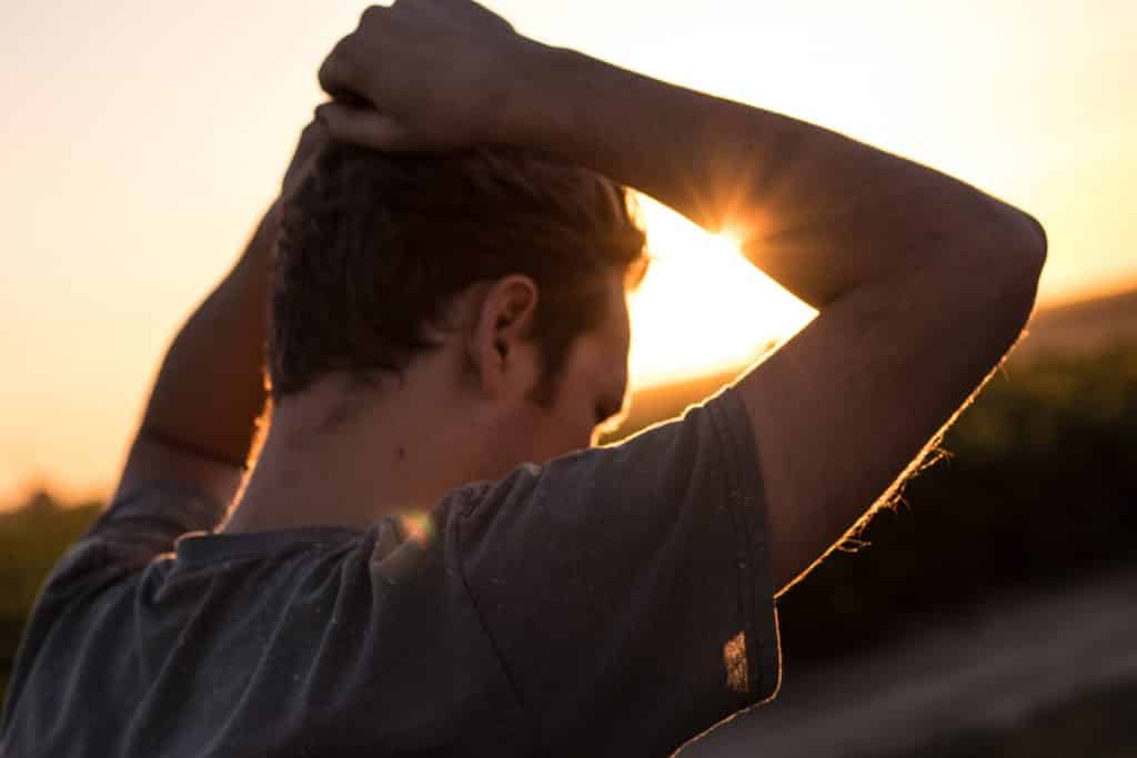 Homem com suas mãos na cabeça em direção ao pôr do sol