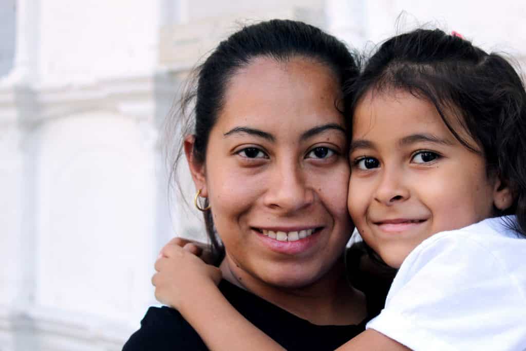 Mãe e filha abraçadas olhando para a câmera.