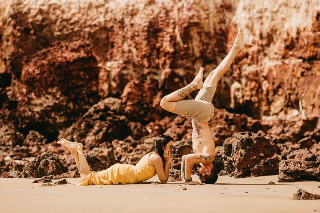 Homem em posição de yoga enquanto a namorada está olhando pra ele.