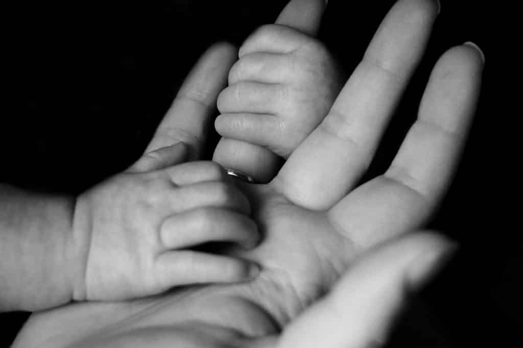 Mãos de um bebê segurando os dedos da mão de uma mulher.