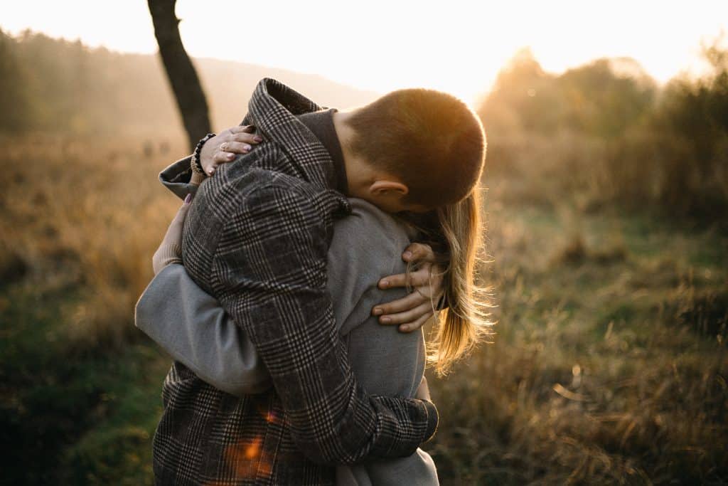 Casal abraçado em um parque natural, sob o pôr do sol.