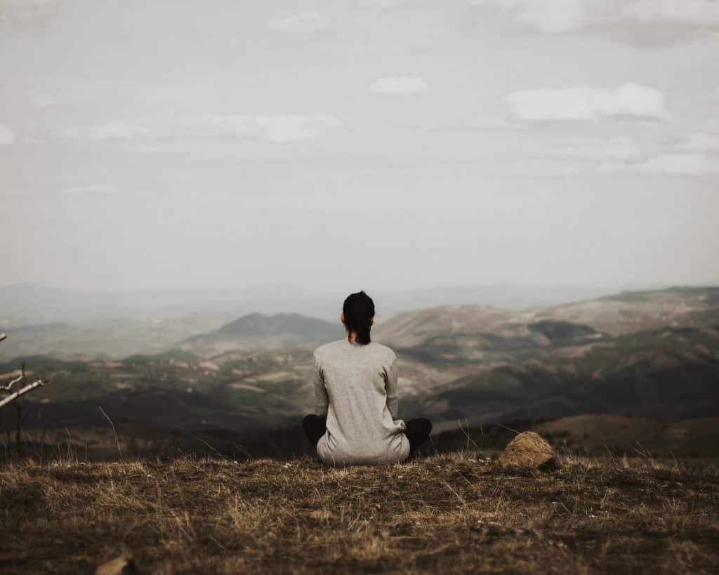 Mulher sentada em uma montanha observando ao seu redor outras montanhas