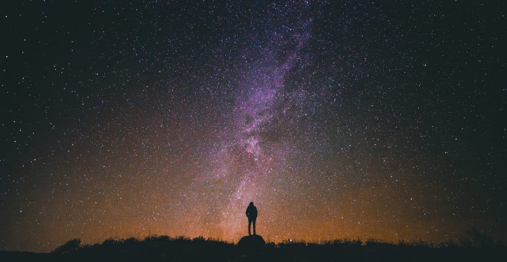 Silhueta de uma pessoa em pé em meio a um céu estrelado.