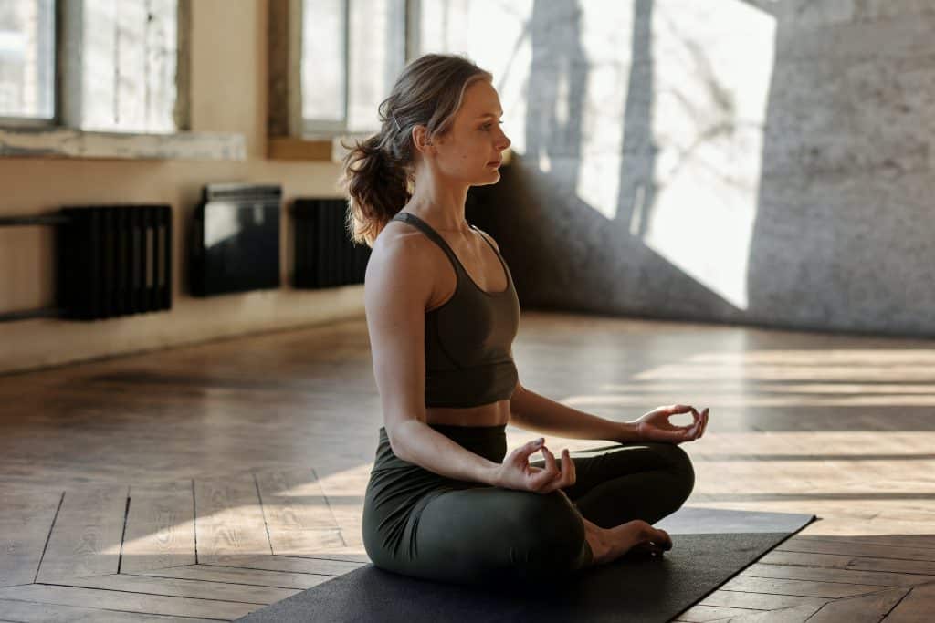 Mulher sentada, de pernas cruzadas, meditando.