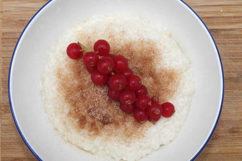 Imagem de arroz doce em um prato de porcelana branco. Ele está pronto para ser servido com canela e frutas vermelhas.