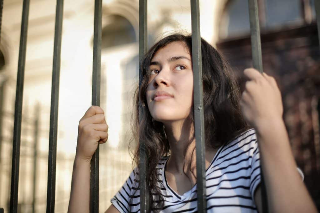 Mulher jovem de cabelos ondulados olhando pelas grades de uma construção.