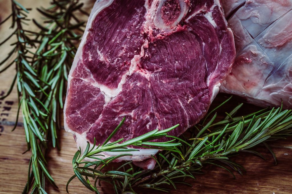 Imagem de uma carne em formato de bife ainda crua. Ao lado dela ramos de alecrim.