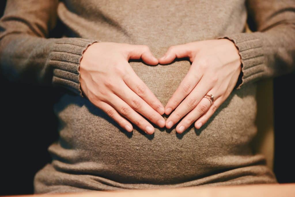 Mulher fazendo coração em cima da sua barriga de grávida.