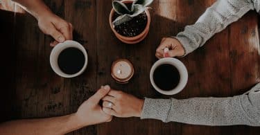 Casal com as mçaos juntas e com a outra mão segurando um café