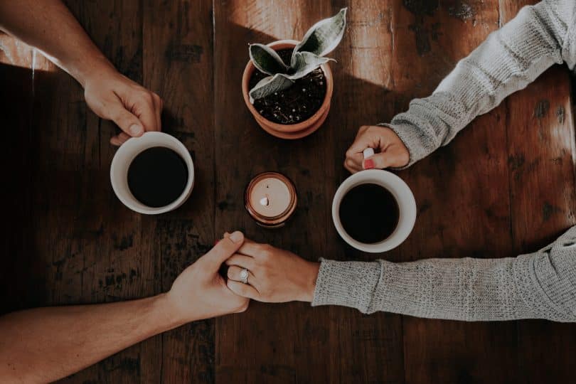 Casal com as mçaos juntas e com a outra mão segurando um café