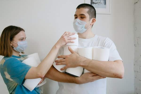 Casal segurando rolos de papel higiênico com máscaras no rosto