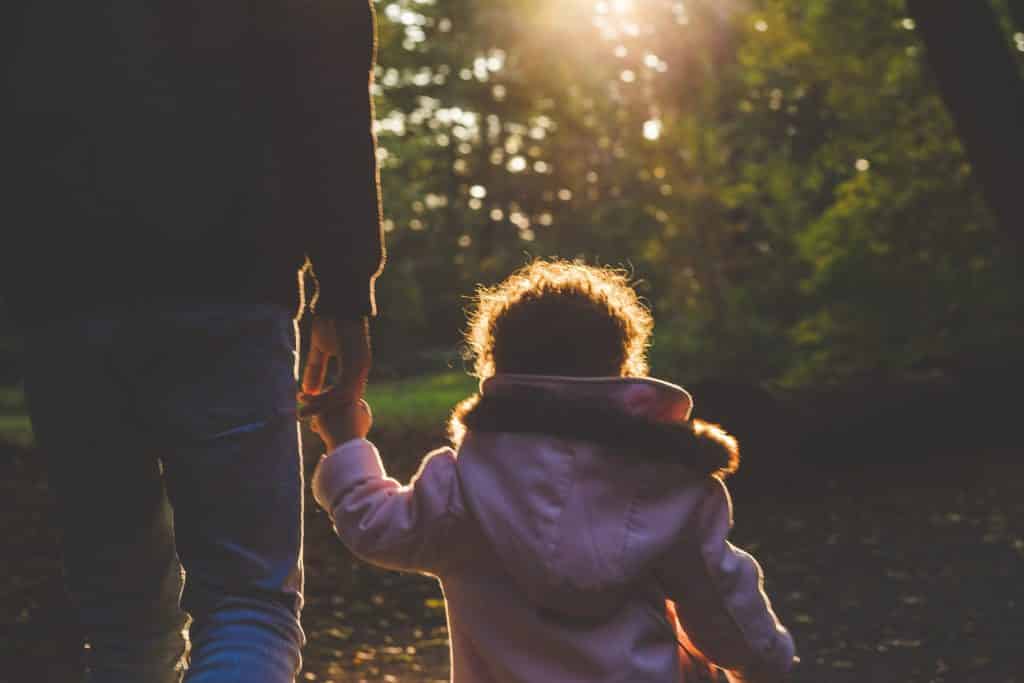 Menina criança andando de mãos dadas com seu pai por um parque.