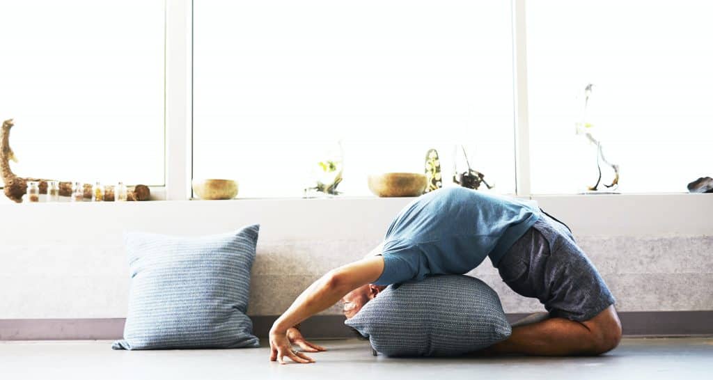 Homem fazendo yoga na sala de sua casa.