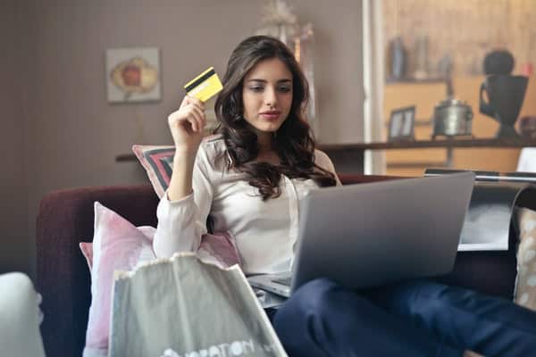 Mulher sentada fazendo compras online com o notebook e cartão na mão