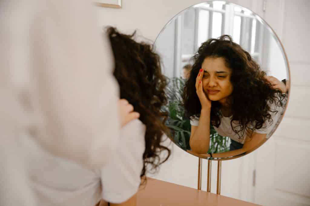 Mulher chorando enquanto olha para o seu reflexo no espelho.