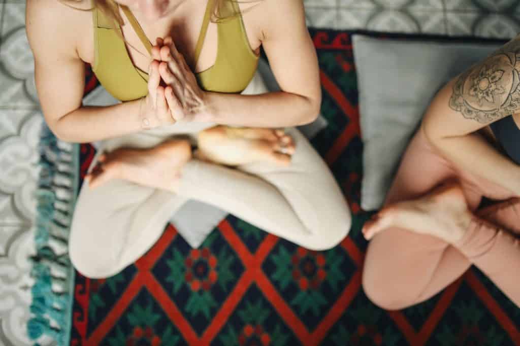 Duas mulheres sentadas de pernas cruzadas praticando yoga.