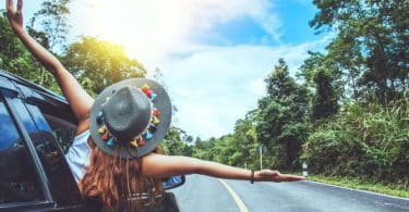 Mulher de braços abertos na janela do carro com estrada ao fundo