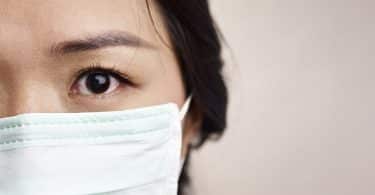 Imagem aproximada de uma mulher de traços sino-asiáticos usando uma máscara de proteção.