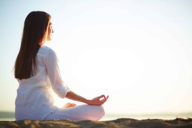 Mulher meditando de pernas cruzadas, de frente para o mar.