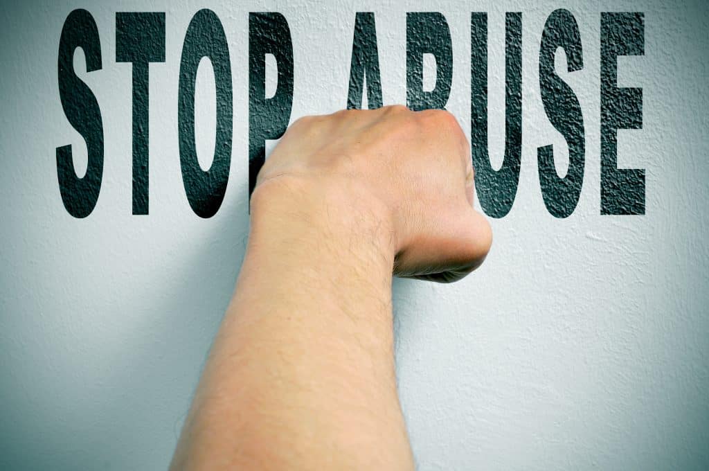 Imagem de um fundo branco e sobre ele está escrito em inglês a palavra STOP ABUSE - pare de abusar - e sobre a palavra a mão de um homem fechada.