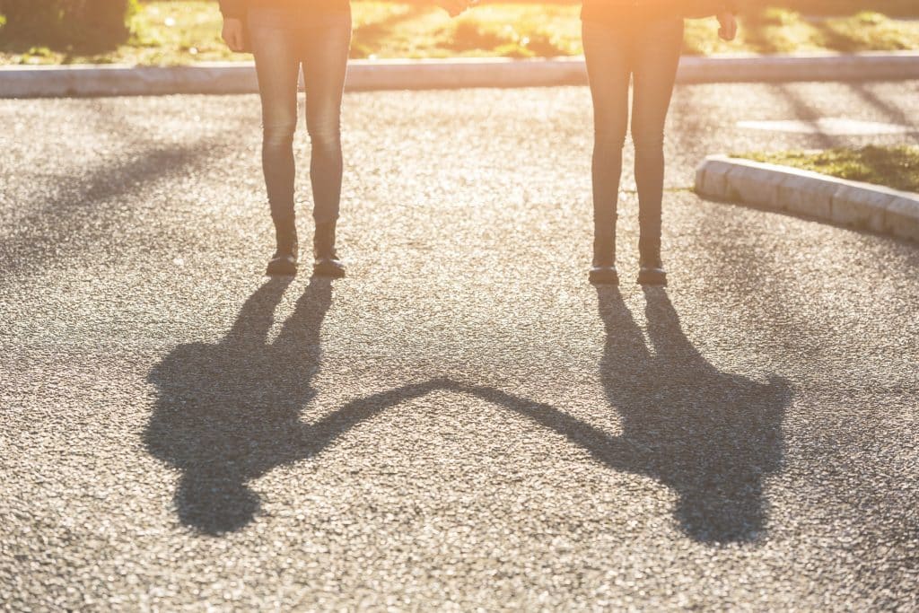Duas pessoas de mãos dadas com suas sombras refletindo no chão