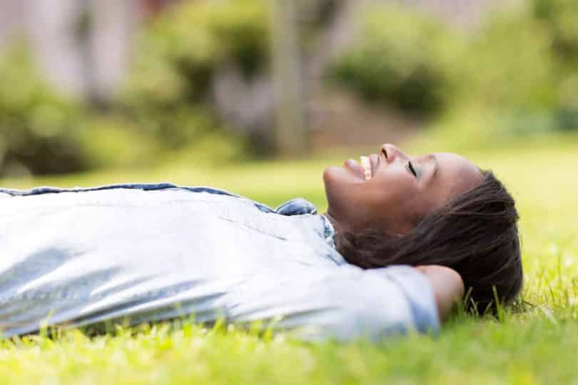 Mulher deitada em gramado com olhos fechados vista de perfil