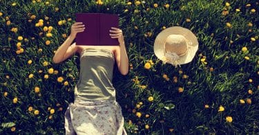 Mulher deitada em um gramado com flores lendo um livro