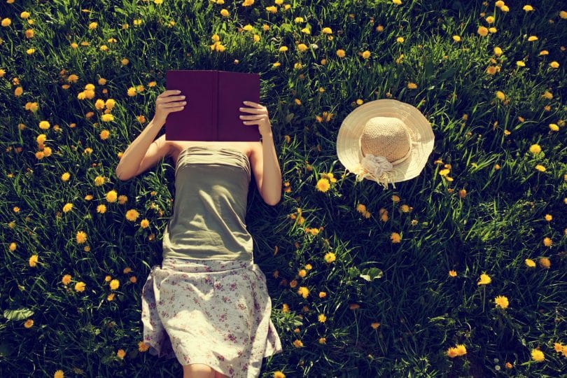 Mulher deitada em um gramado com flores lendo um livro