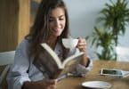 Mulher em sua mesa lendo livro e tomando café