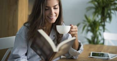Mulher em sua mesa lendo livro e tomando café