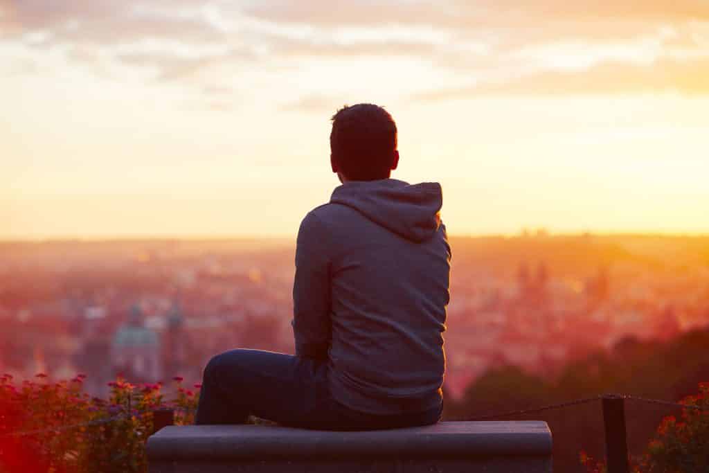 Homem sentado no topo de um prédio olhando para o pôr do sol