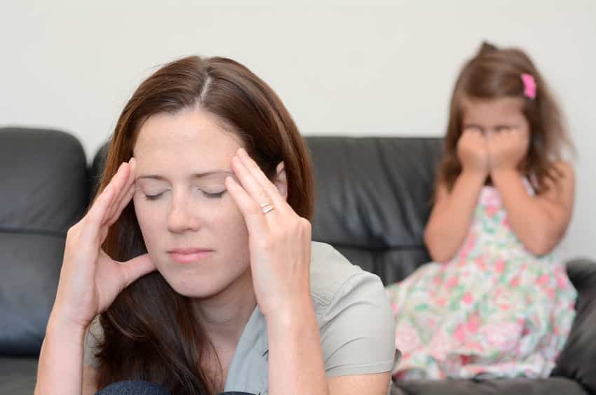 Mãe nervosa com filha chorando ao fundo da foto