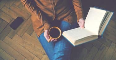 Mulher lendo livro segurando uma xícara de café