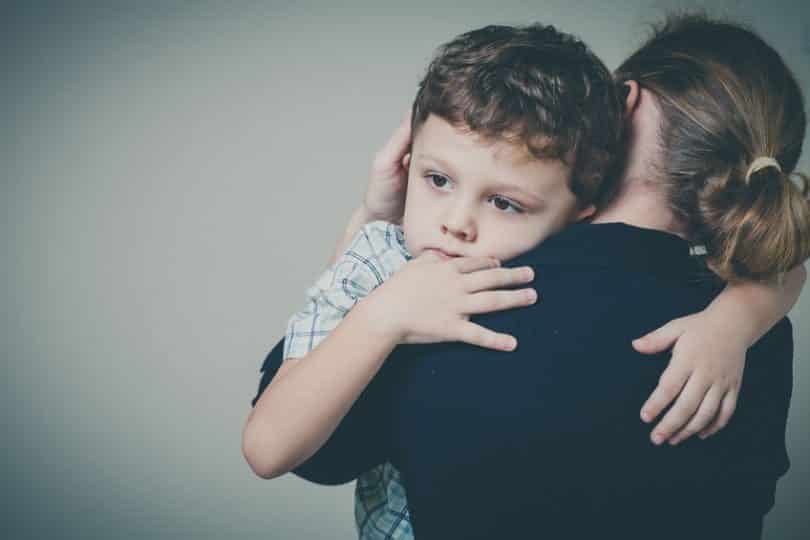 Mãe de costas com filho no colo com expressão triste