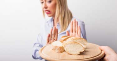 Mulher com as duas mãos em frente ao seu corpo e a uma bandeja com pão.
