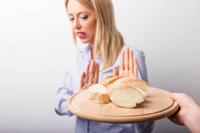 Mulher com as duas mãos em frente ao seu corpo e a uma bandeja com pão.