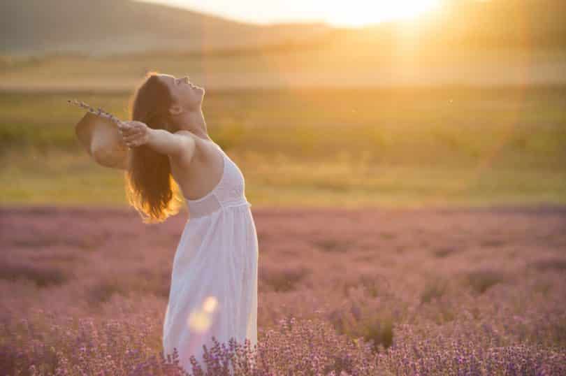 Mulher de perfil com braços abertos em campo com sol refletindo