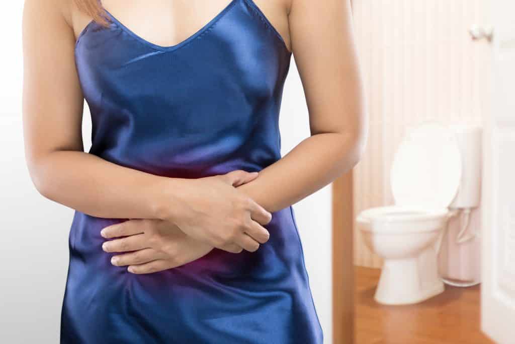 Imagem do corpo de uma mulher vestindo uma camisola de cetim azul. Ela está com as duas mãos sobre a região da barriga. Ela foi diagnosticada com o útero bicorno.