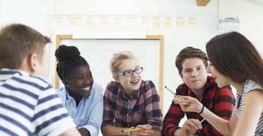 Grupo de alunos sentados ao redor de uma mesa, conversando.