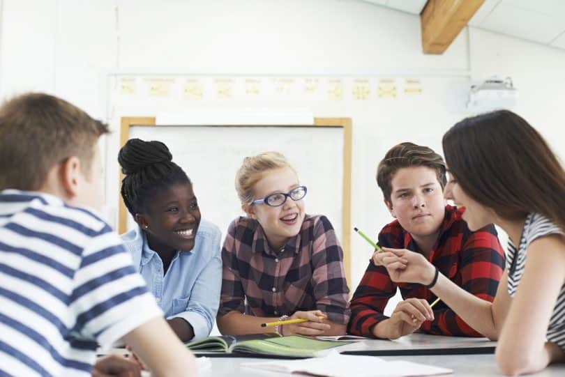 Grupo de alunos sentados ao redor de uma mesa, conversando.