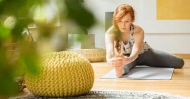 Mulher praticando yoga em um tapete, na sala de casa.