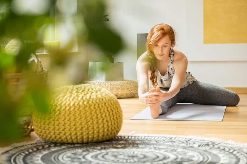 Mulher praticando yoga em um tapete, na sala de casa.