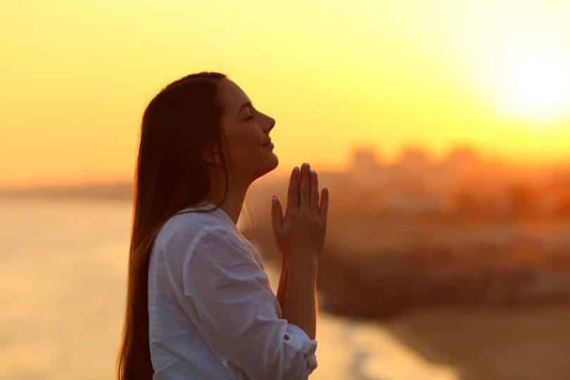 Mulher com mãos em frente ao corpo unidas e pôr-do-sol ao fundo