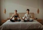 Imagem de um casal meditando no quarto, sobre a cama.