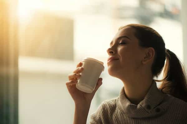 Mulher tomando café de olhos fechados e sol refletindo