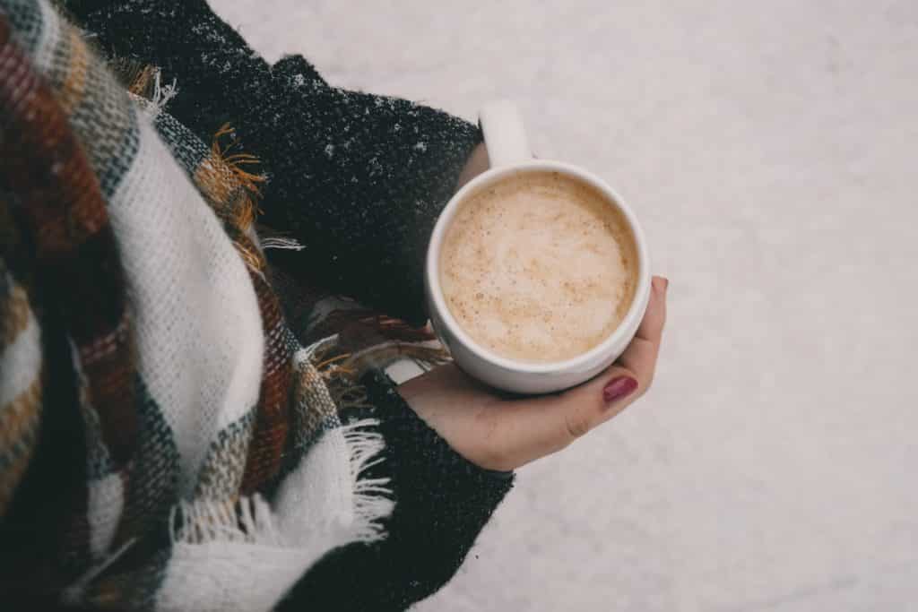 Pessoa com roupas de frio segurando uma xícara de café quente.